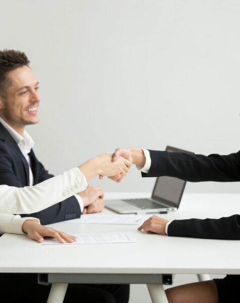 Smiling diverse businesswomen shake hands at group meeting, friendly asian hr handshaking congratulating hired applicant at job interview, satisfied millennial partners make contract deal concept